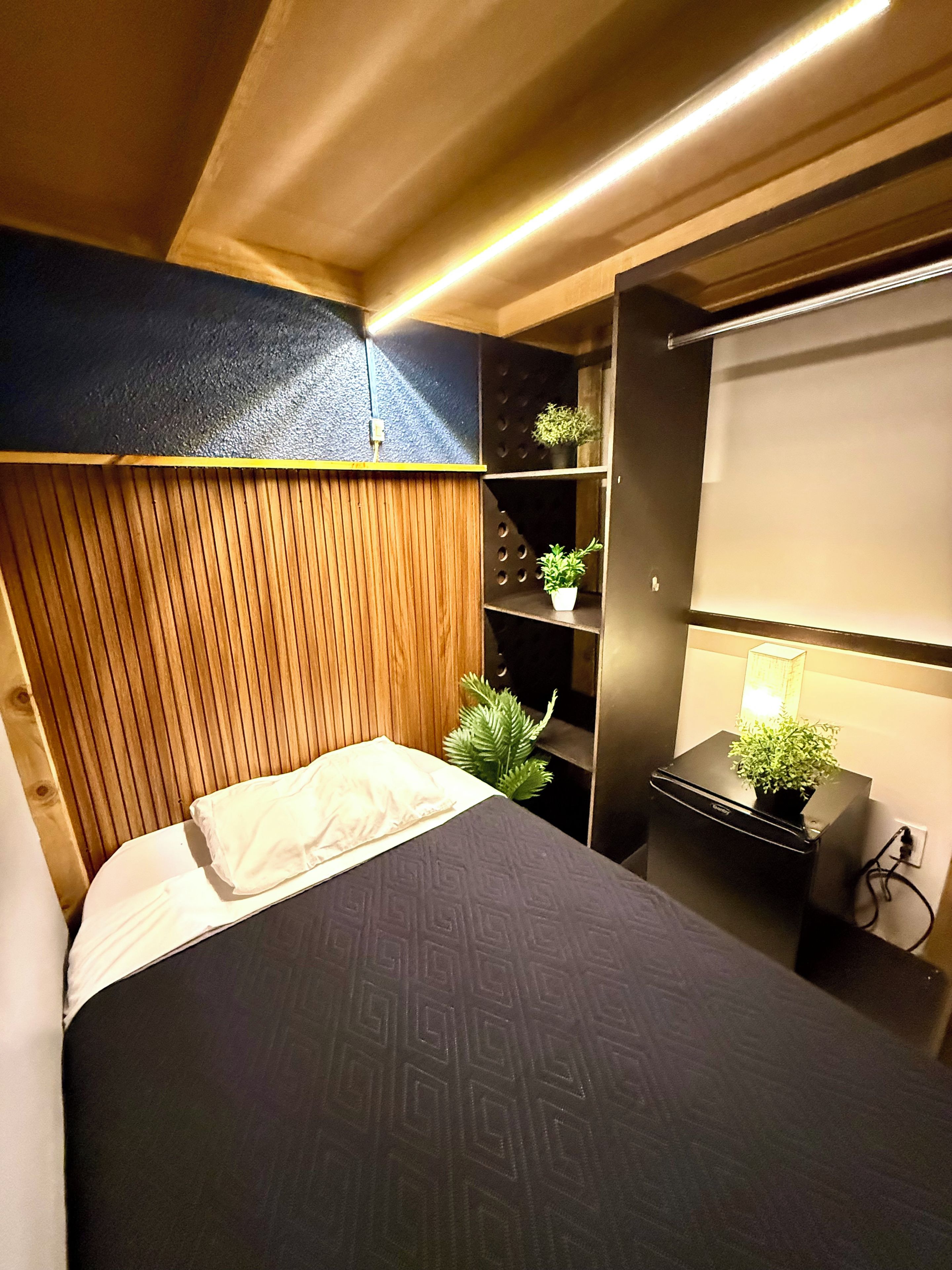 A modern bedroom with a bed, a nightstand with a lamp, and a potted plant.