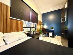 Une chambre d’hôtel moderne, équipée d’un lit, d’un bureau, d’une chaise et offrant une vue sur l’extérieur.