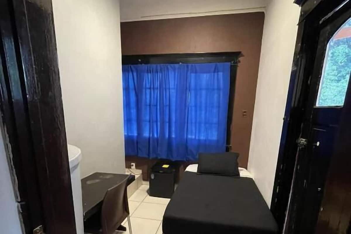 A small, compact room with a bed, a desk, and a chair.