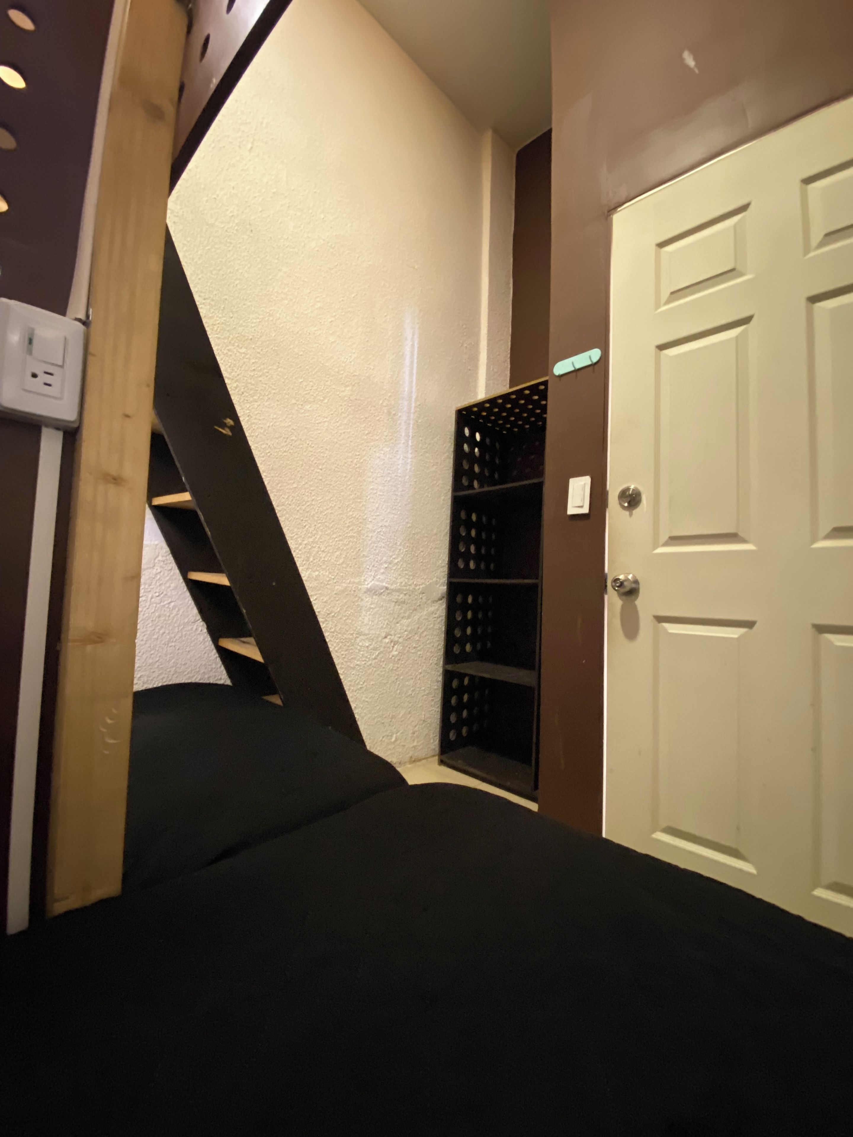 A narrow stairway leading to a lower level, a white door, and a black shelving unit against the wall.