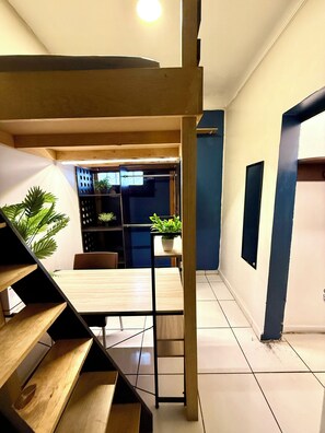 A staircase leading to a dining area with a table and chairs, surrounded by potted plants and a blue wall. - Urban Rooms - Hostel (Mexico City)
