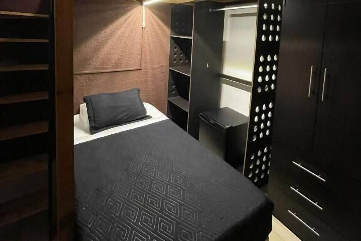 A bunk bed with a headboard, a bedside table, a wardrobe with a mirror, and a small seating area.