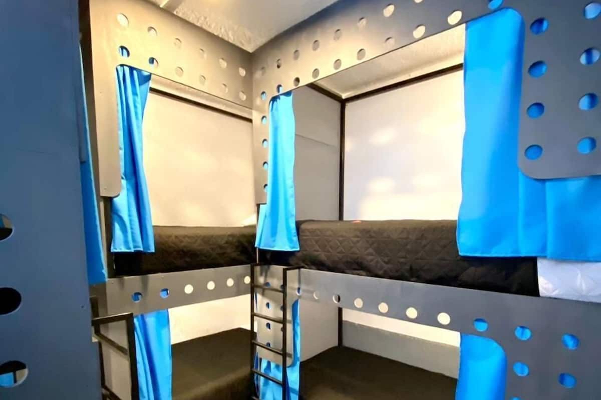 A bunk bed room with a ladder, a curtain, and a wall with circular cutouts.