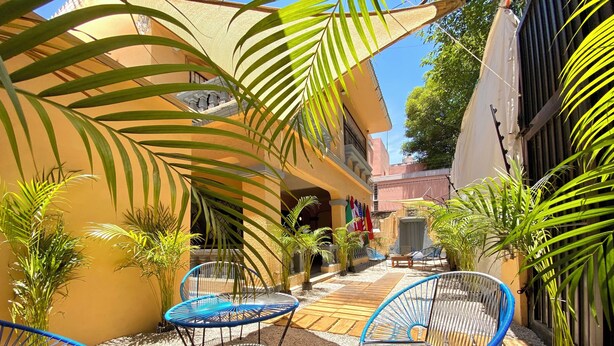 A courtyard with outdoor seating, palm trees, and a building facade. - RMS Hostal - Roma (Mexico City)