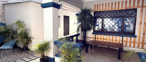 A covered outdoor area with a wooden deck, potted plants, and a bench.