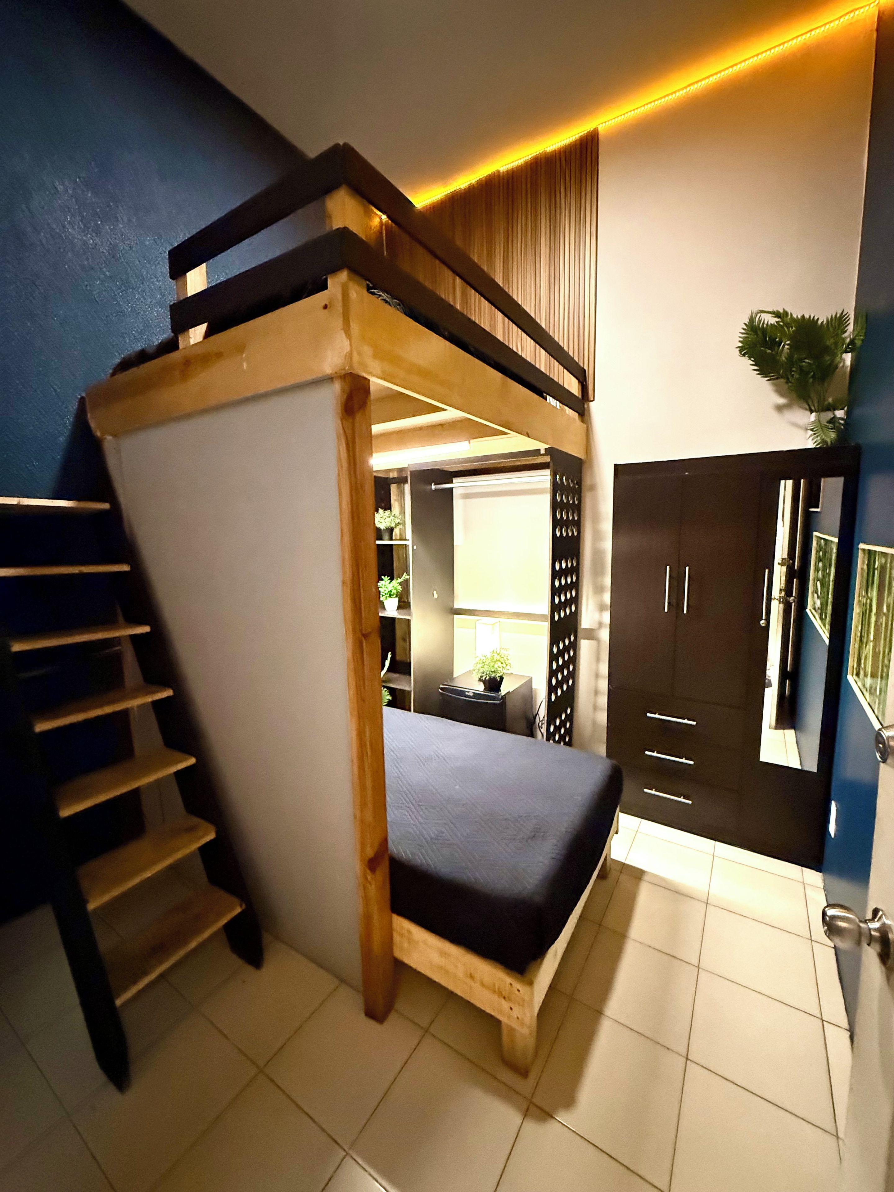 Un lit superposé avec une échelle en bois, un bureau avec une plante et une armoire avec un miroir.