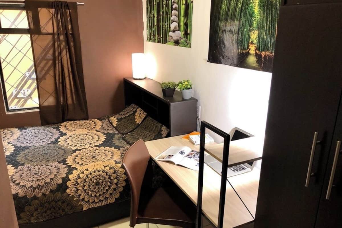 A bedroom with a bed, a desk, a chair, a lamp, and a wardrobe.