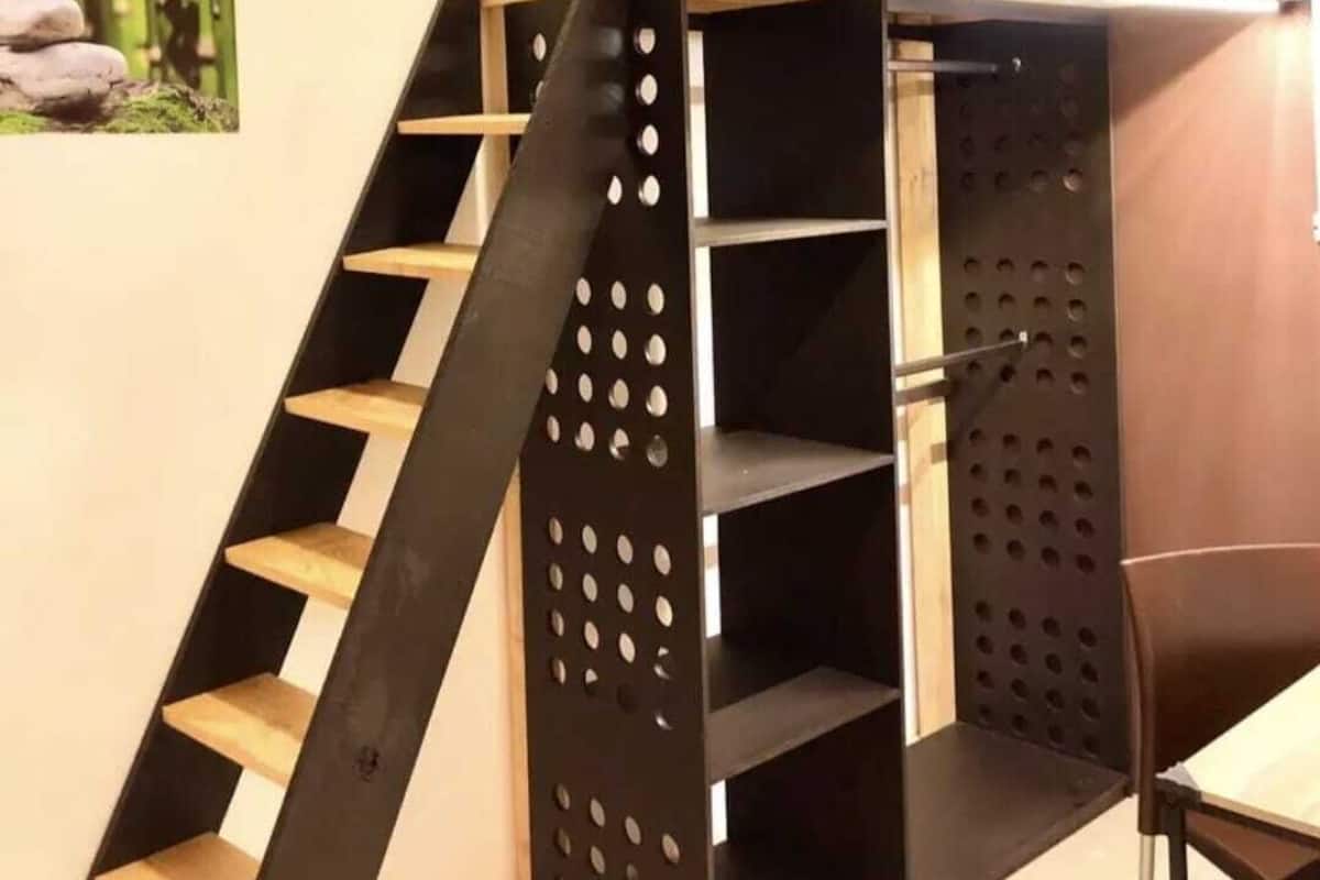 A bunk bed with a wooden ladder and shelves, a small table, and a picture of stones on the wall.