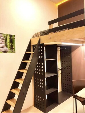 A bunk bed with a wooden ladder and shelves, a small table, and a picture of stones on the wall. - RMS Hostal - Roma (Mexico City)