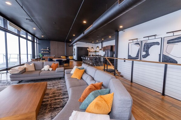 Uma sala de estar moderna com sofá seccional cinza, mesa de centro de madeira e uma grande janela que oferece luz natural.