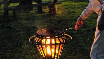 A person cooking outdoors with a metal fire pit.