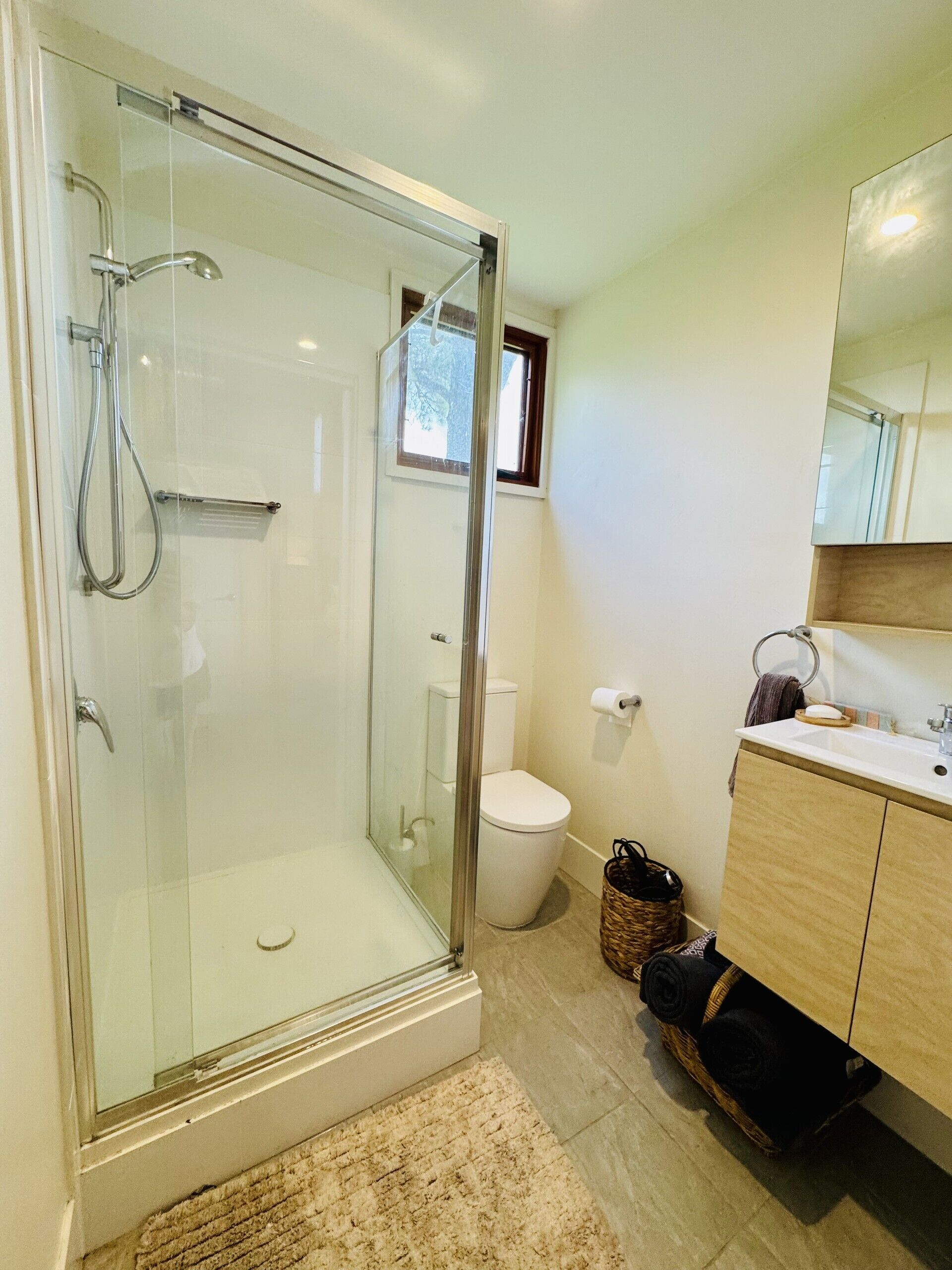 A modern bathroom with a glass-enclosed shower, a toilet, and a wooden vanity with a mirror.