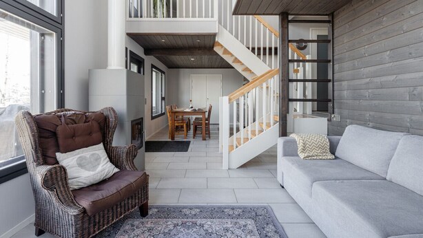 A spacious living area with a high ceiling, a staircase leading to an upper level, a dining area, and a grey sofa. - Spacious & Cozy 2BR Cabin at Riihivuori Peak next to Ski Slopes (Muurame)