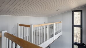 A high ceiling with visible wooden beams, a white railing, and a window with a view of trees. - Spacious & Cozy 2BR Cabin at Riihivuori Peak next to Ski Slopes (Muurame)