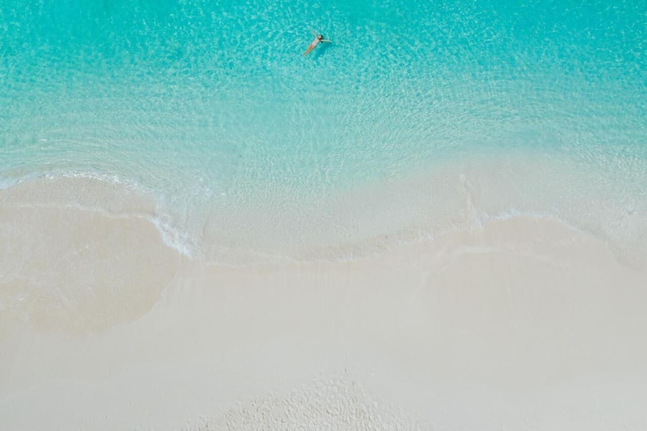 A beach with clear turquoise water and a person swimming.