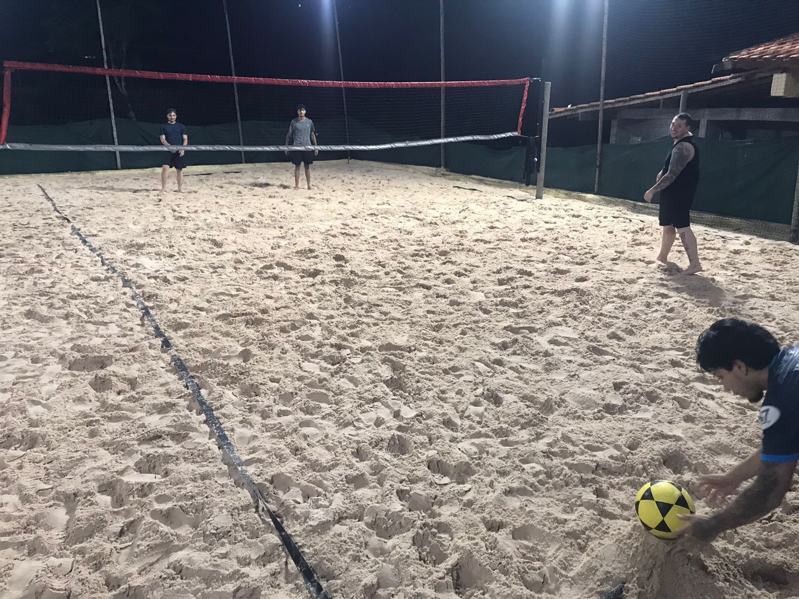 Una cancha de voleibol al aire libre con red, arena y jugadores.
