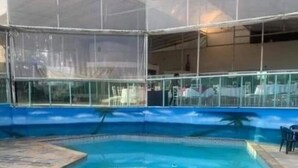 A swimming pool with a blue border and a covered area with a glass barrier. - Arena da serra beach tennis espaço fest (Itapecerica da Serra)