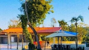 A building with a red roof, a covered outdoor seating area, and a fenced area with chairs. - Arena da serra beach tennis espaço fest (Itapecerica da Serra)