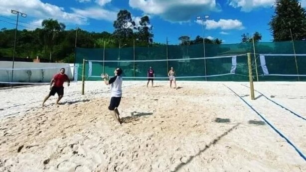 A beach volleyball court with a net, sand, and trees in the background. - Arena da serra beach tennis espaço fest (Itapecerica da Serra)