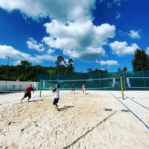 En strandvolleyballbane med net, sand og træer i baggrunden.