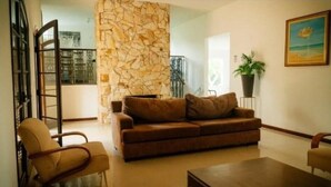 A living room with a brown sofa, a wooden coffee table, and a beige armchair. - Arena da serra beach tennis espaço fest (Itapecerica da Serra)