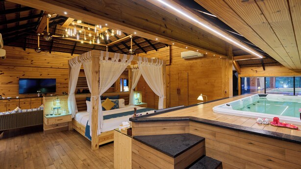 Une cabane en bois dotée d’un jacuzzi à ciel ouvert, d’un lit à baldaquin et d’un téléviseur placé dans un coin.