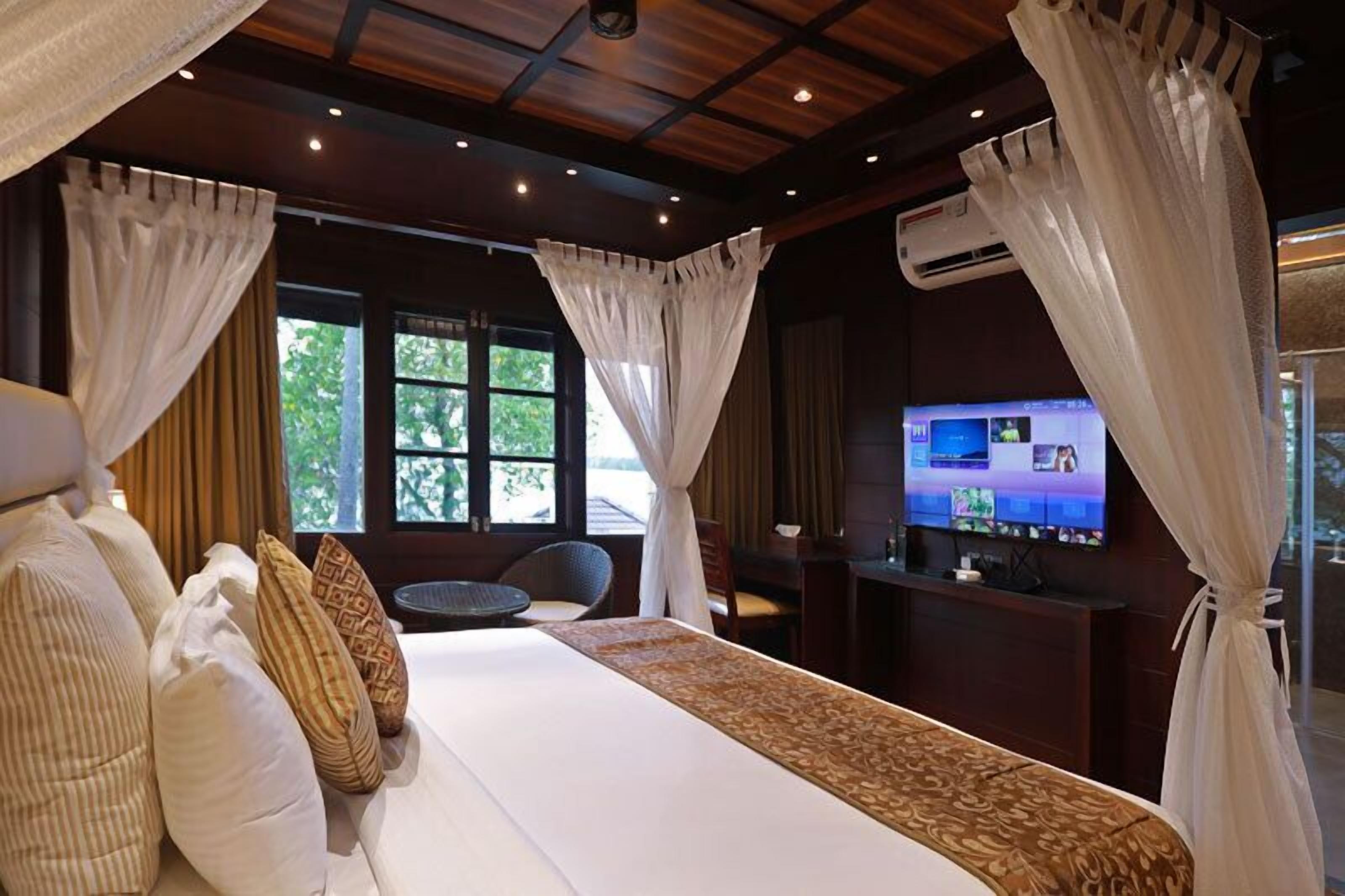 A hotel room with a large bed, a TV, and a window with curtains.