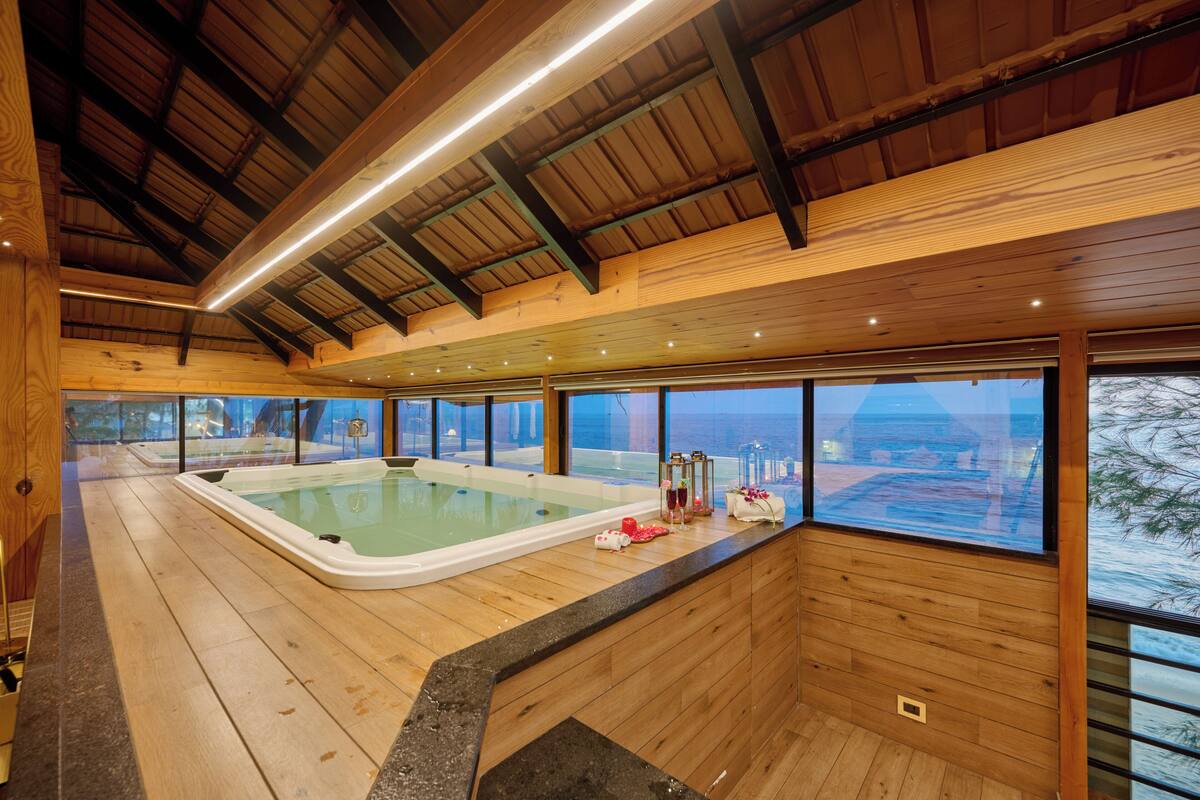 Un intérieur en bois avec un jacuzzi et de grandes fenêtres donnant sur un plan d’eau.