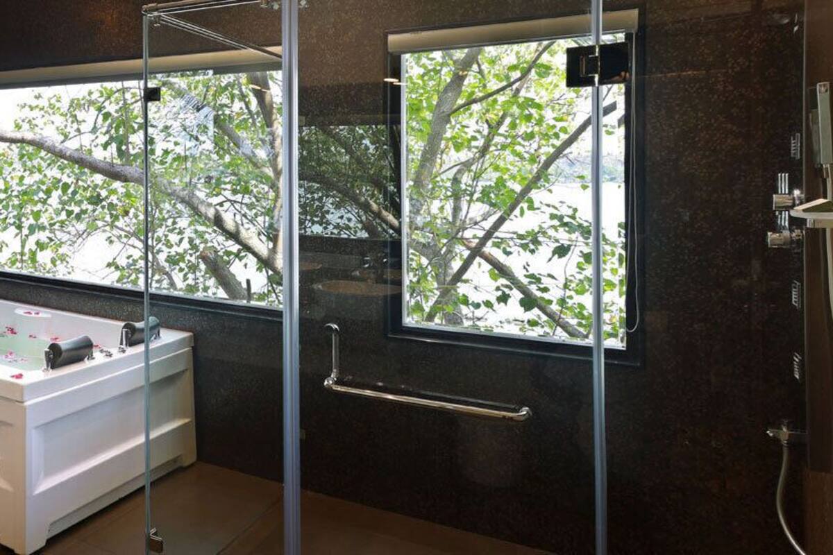 Une salle de bain moderne dotée d’une grande baignoire, d’une cabine de douche en verre et d’une fenêtre donnant sur la verdure.