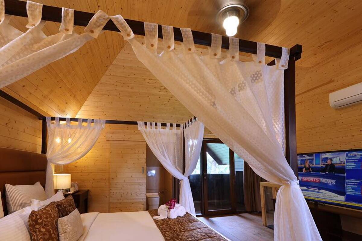 Une chambre dans une cabane en bois, avec un lit, des tables de chevet et un téléviseur diffusant des informations sportives.