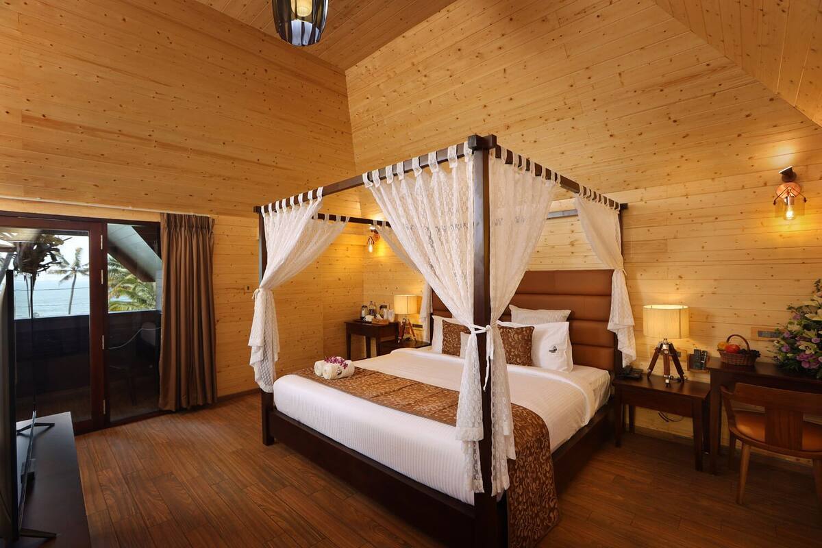 Un lit à baldaquin, un parquet en bois, un bureau avec une chaise et une vue à travers une porte vitrée.