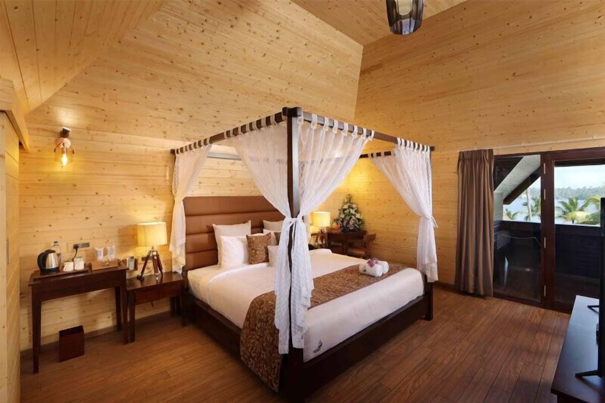 Une chambre à coucher de style cabane en bois, avec un lit à baldaquin, une table de chevet, une lampe et une vue sur l’extérieur grâce à une porte coulissante.