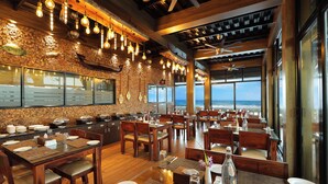 Un restaurant avec des tables et des chaises en bois, des luminaires suspendus et une vue sur l’océan.