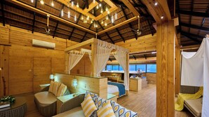 Une cabane en bois comprenant un lit, un coin salon et une cloison en verre.