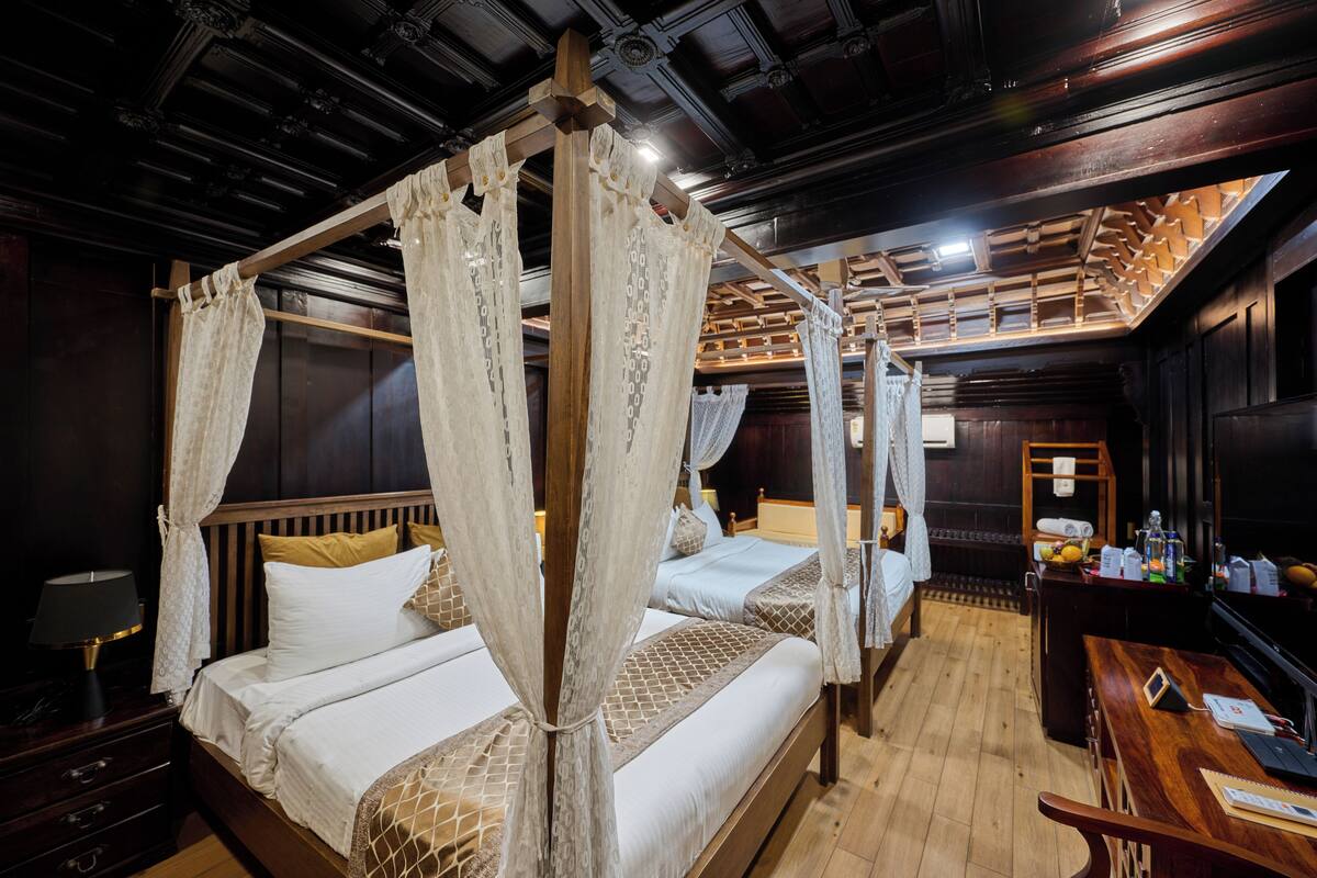 Une chambre avec deux lits, chacun doté d’un baldaquin, de têtes de lit en bois et d’un bureau en bois avec une chaise.