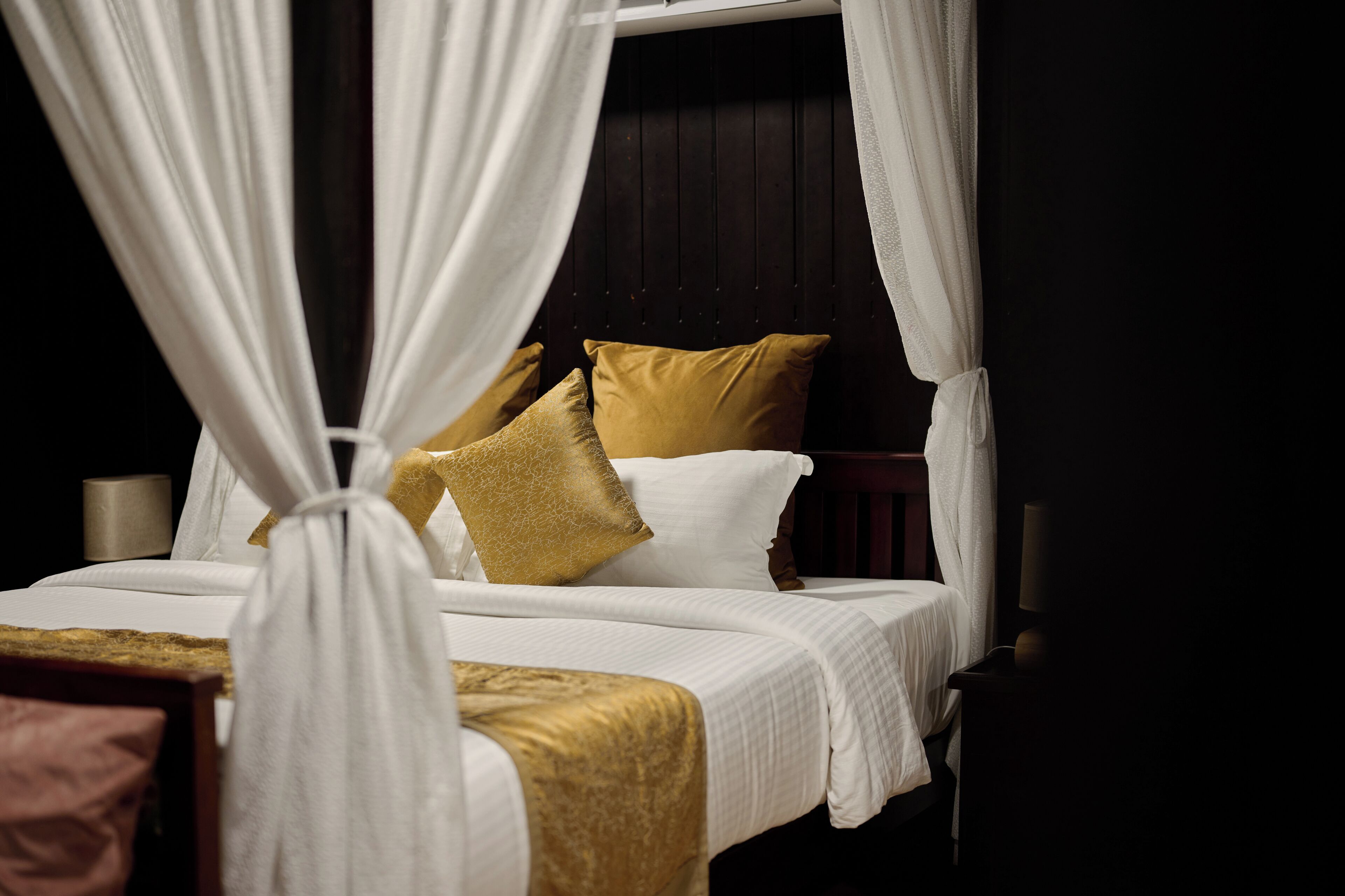 Una cama con ropa blanca, un edredón dorado y un dosel.