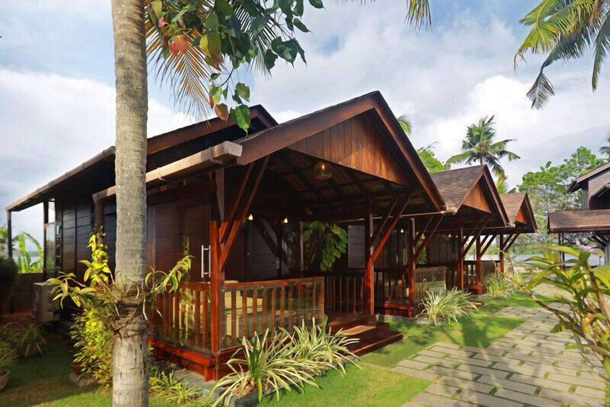 Une cabane en bois dotée d’une véranda, entourée de plantes tropicales et de palmiers.