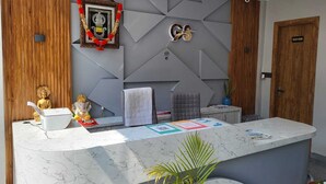 Ein Empfangstresen mit Marmorplatte, ein gerahmtes Bild einer Gottheit, eine Buddha-Statue und ein Schild mit der Aufschrift 'Wash Room'.