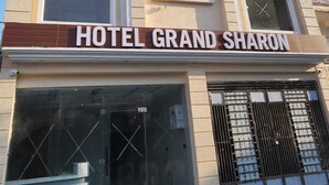 Ein mehrstöckiges Hotel namens "Hotel Grand Sharon" mit einer modernen Fassade, großen Fenstern und einem gut sichtbaren Eingang.