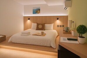 Ein modernes Hotelzimmer mit einem ordentlich bezogenen Bett, einem kleinen Nachttisch mit einer Lampe, einer Topfpflanze und Blick auf das Meer durch das Fenster.