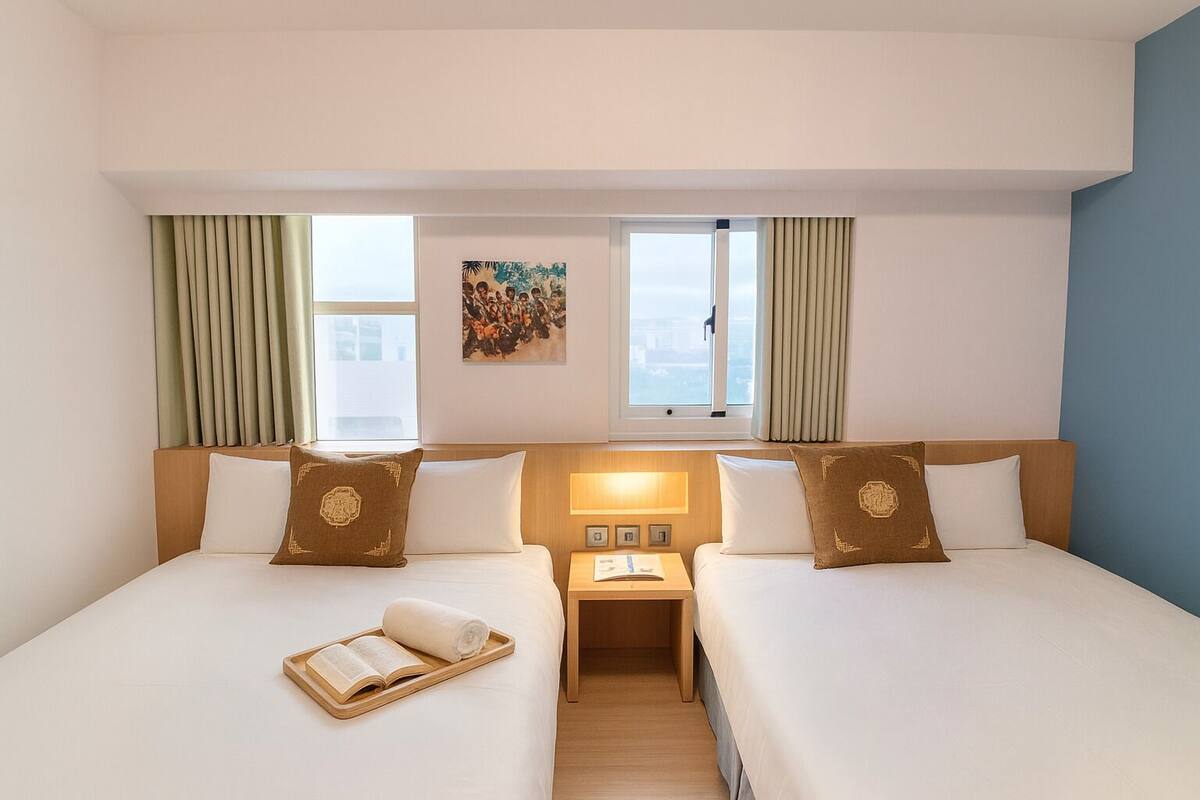Een hotelkamer met twee bedden, een nachtkastje, een raam en een schilderij aan de muur.
