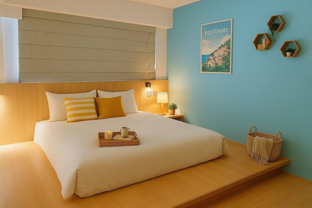 Een net opgemaakt bed met een dienblad, een hoofdbord, een muur met een poster en een kleine tafel met een lamp.