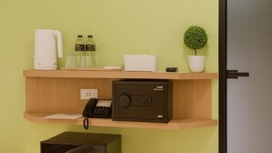 Une pièce avec un bureau en bois, une radio noire, un climatiseur blanc, une petite plante en pot, une bouilloire blanche et une paire de pantoufles noires.
