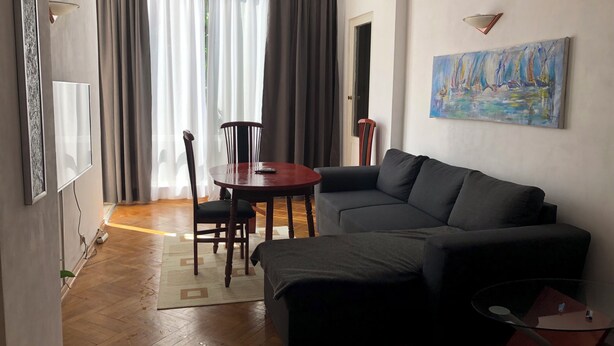 Un salón con sofá, una mesa redonda y una silla. Hay un cuadro en la pared y un equipo de aire acondicionado montado en la pared.