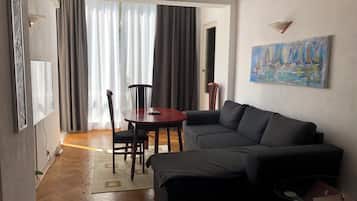 Ein Wohnzimmer mit einer Couch, einem runden Tisch und einem Sessel. An der Wand hängt ein Bild und eine Klimaanlage ist an der Wand montiert.