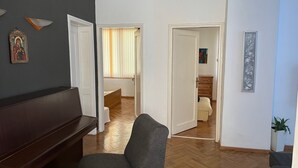 Una sala de estar con un sofá marrón oscuro, un sillón gris y piso de madera. Hay dos puertas que dan a otras habitaciones, una con una cama y la otra con un aparador.