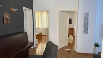 Ein Wohnzimmer mit einem dunkelbraunen Sofa, einem grauen Sessel und Holzboden. Zwei Türen führen in andere Räume, eine zum Schlafzimmer und die andere zum Ankleidezimmer.