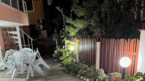 Un camino de concreto que lleva a un área cerrada con valla de madera y plantas en macetas.