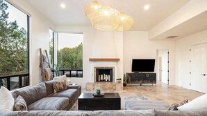 A spacious living room with a fireplace, large windows, and a modern chandelier. - Enchanted Waters Retreat (Sedona)