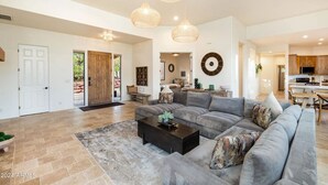 A spacious living room with a large sectional sofa, a coffee table, and a dining area with wooden furniture. There is a kitchen in the background with modern appliances. - Enchanted Waters Retreat (Sedona)